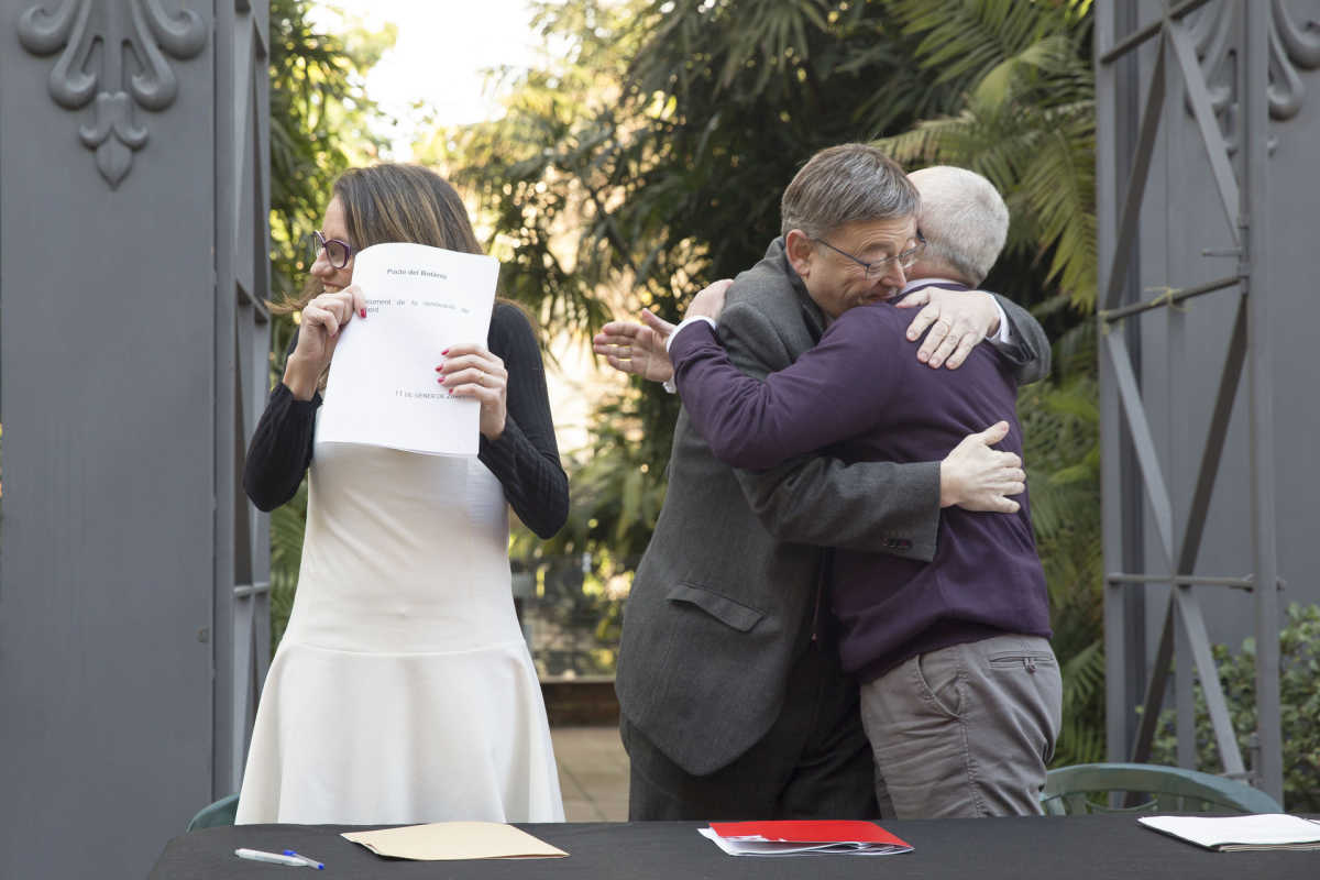 Puig y Montiel se abrazan tras la renovación del Pacto del Botánico mientras Oltra muestra el documento. Foto: EVA MÁÑEZ